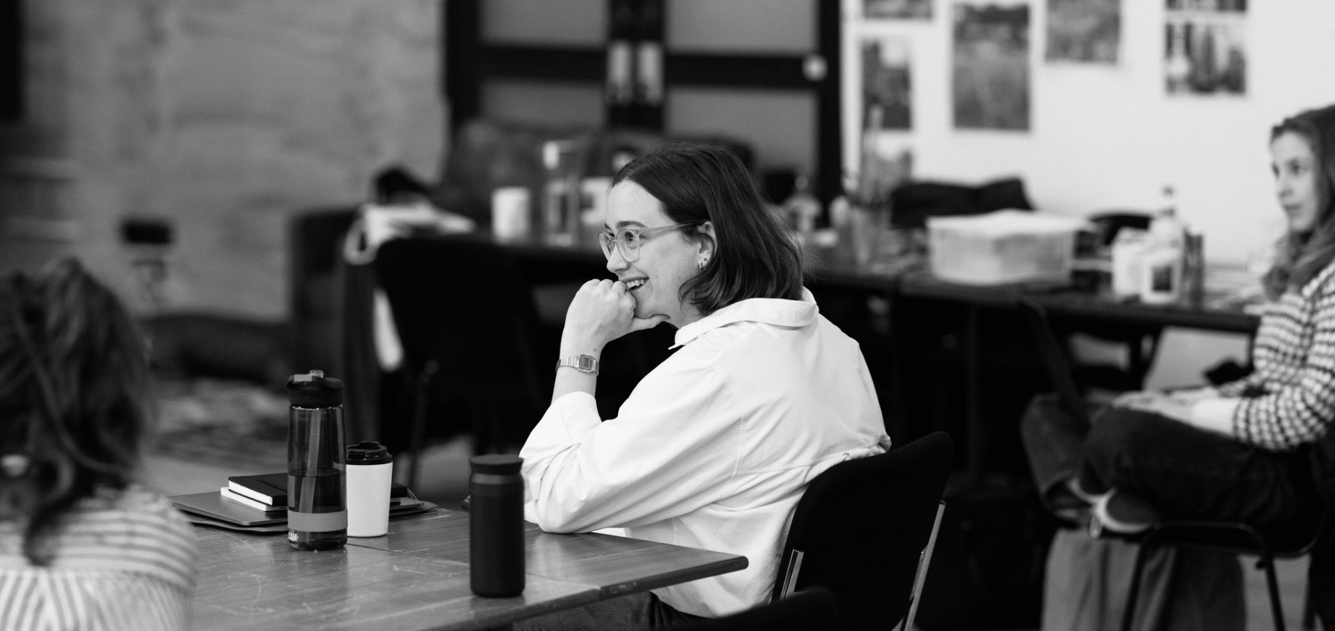 A white woman with brunette hair and glasses smiles in a rehearsal room